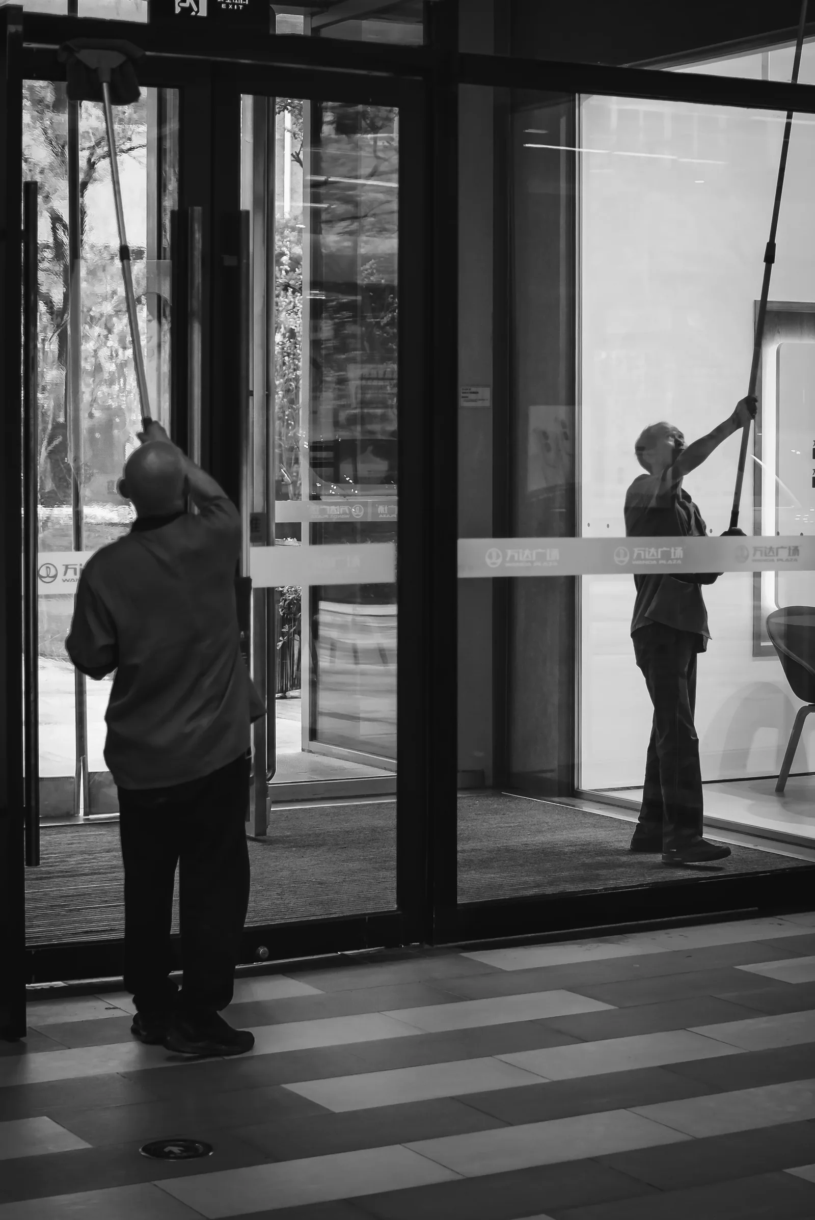 Dos profesionales realizando limpieza de cristales en el acceso de un edificio comercial