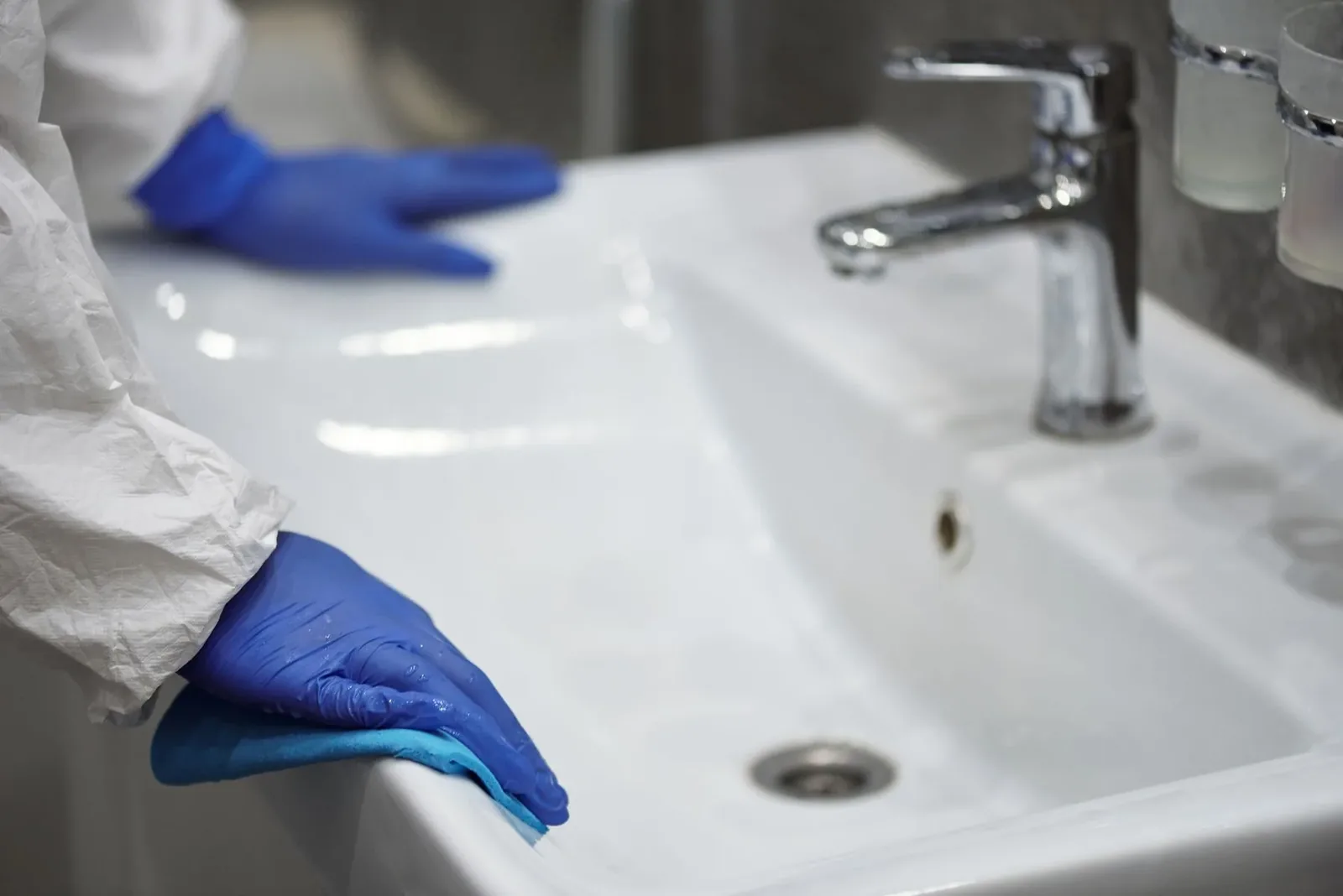 Manos con guantes limpiando un lavamanos blanco